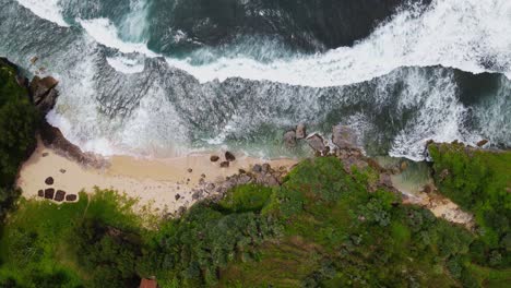 Static-drone-shot-of-tropical-beach-surrounded-by-forest-and-hill-with-big-sea-waves---Indonesia,-Asia