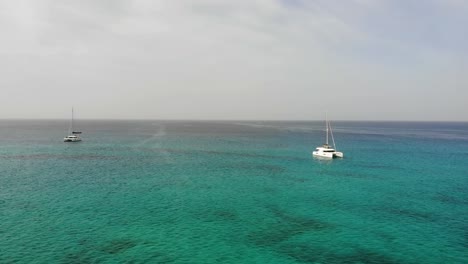 Vista-Aérea-Sobre-Las-Hermosas-Aguas-Turquesas-Del-Océano-Con-Dos-Catamaranes-Navegando-En-Sal-Cabo-Verde
