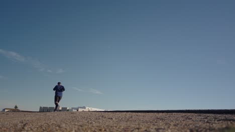 Runner-running-road,-low-angle-back-view,-blue-sky-and-empty-roadway,-healthy-lifestyle