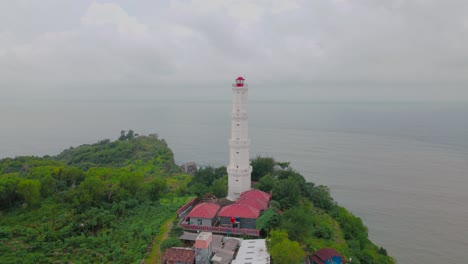 Orbit-drone-shot-of-old-white-lighthouse-on-the-top-of-coral-cliff-border-with-sea---Baron-Beach,-Indonesia