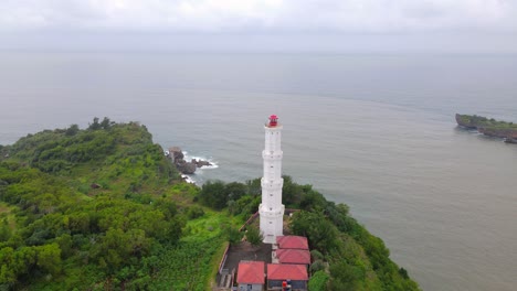Aerial-view-of-coral-cliff-overgrown-by-trees-with-white-lighthouse-build-on-it---Baron-Beach,-Indonesia