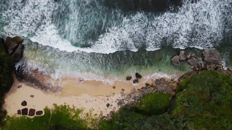 Static-drone-shot-of-big-sea-wave-on-the-tropical-beach-surrounded-by-trees---Indonesia,-Asia
