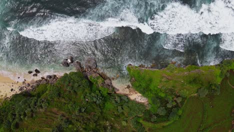 Overhead-drone-shot-of-Big-waves-on-the-beach-hitting-the-rocky-shore-cliffs---Tropical-beach-of-Indonesia