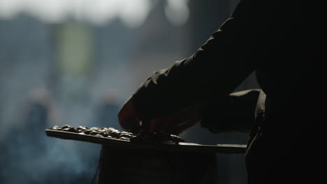 Vendedor-Coloca-Castañas-En-Horno-Caliente,-Primer-Plano,-Toma-De-Silueta