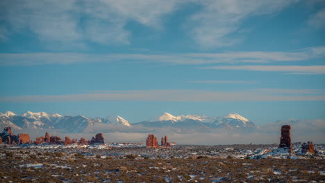 Timelapse-of-Arches-National-Park,-Red-Sandstone-Formations-in-Valley-Under-Snow-Capped-Peaks