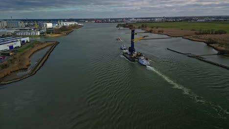 High-up-landscape-aerial-shot-of-a-towboat-pushing-a-raft-carrying-a-big-industrial-crane-over-water,-Ahoy,-Zwijndrecht