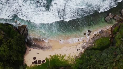 Static-drone-shot-of-big-sea-wave-on-the-tropical-beach-surrounded-by-trees