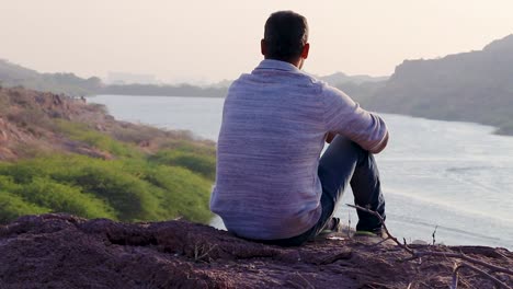 Isolierter-Junger-Mann-Sitzt-Auf-Einem-Berggipfel-Mit-Seeblick-Aus-Flachem-Blickwinkel.-Das-Video-Wurde-Am-Kaylana-See-In-Jodhpur,-Rajasthan,-Indien,-Aufgenommen
