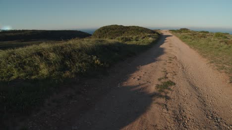 An-empty,-dusty-path-leading-to-a-cliff-alongside-wild-grass-waving-in-the-wind
