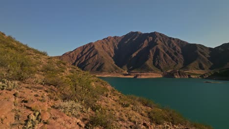 Aeril-dolly-over-a-hill-revealing-a-tropical-lake-and-vast-mountain-range-in-Mendoza