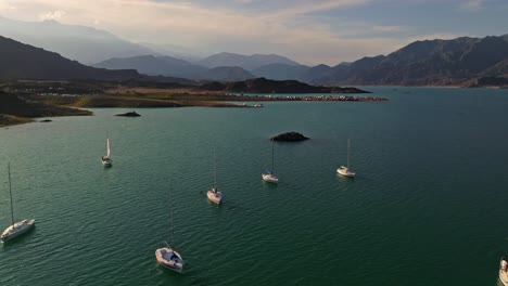 Aerial-shot-overhead-a-group-of-sailboats-with-a-campsite-in-the-background,-Mendoza
