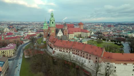 Establishing-drone-aerial-shot-of-Krakow-Wawel-Royal-Castle-moving-backwards,-city-center-fortress-with-the-old-town-and-Cracow-skyline-at-sunset