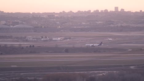 Airplanes-in-Madrid-airport-taxiway-during-sunset-with-city-skyline-as-background