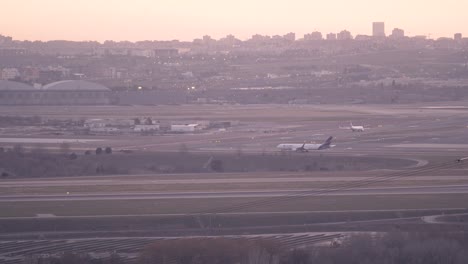 Aviones-En-La-Pista-De-Rodaje-Del-Aeropuerto-De-Madrid-Durante-La-Puesta-De-Sol-Con-El-Horizonte-De-La-Ciudad-Como-Fondo