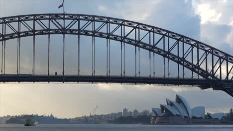 Un-Tren-Pasa-Sobre-El-Puente-Del-Puerto-De-Sydney-Mientras-Un-Ferry-Pasa-Por-Debajo,-En-Australia