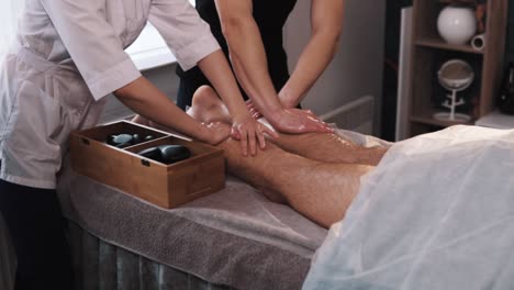 Hände-Männlicher-Und-Weiblicher-Massagetherapeuten-Massieren-Die-Beine-Eines-Mannes-In-Sportkleidung-Mit-Der-Vierhandtechnik