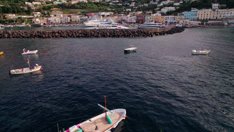 Eine-Filmische-Weitwinkel-Drohnenaufnahme,-Die-Sich-Vom-Wasser-Aus-Nach-Oben-Neigt-Und-Sich-Marina-Grande-Auf-Der-Insel-Capri-In-Kampanien,-Italien,-Nähert,-Mit-Booten-Im-Berühmten-Hafen-Und-Einem-Weiten-Blick-Auf-Farbenfrohe-Pastellgebäude