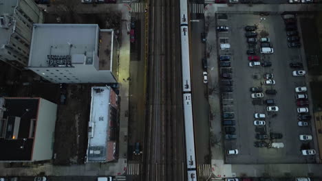 Aerial-view-above-a-train-driving-on-elevated-rails-in-illuminated-New-York,-USA---top-down,-drone-shot