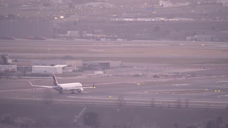 Back-view-of-Airplane-in-Madrid-airport-taxiway-during-sunset-with-city-skyline-as-background