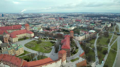 Aerial-view-fliying-over-Wawel-Royal-Castle-by-the-river-Vistula-in-the-city-of-Krakow,-Poland,-with-the-city-center-in-the-background