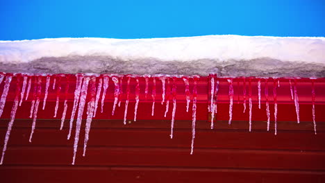 Icicles-melting-on-red-roof-side-on-sunny-winter-day,-fusion-time-lapse