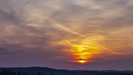 Sun-rising-on-the-horizon-in-a-timelapse-shot-in-a-sky-with-clouds-over-mountains-and-hills-with-trees