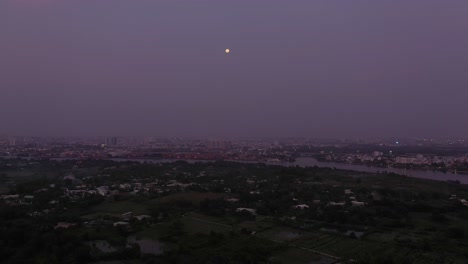Aerial-view-of-Saigon-river-in-the-twilight-with-ambient-and-artificial-light-looking-towards-full-moon
