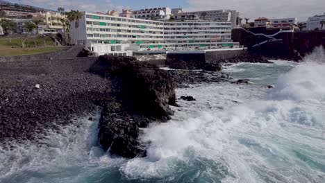 aerial-view-of-hotel-tourist-resort-in-playa-de-piedra-Tenerife-island-Santa-Cruz,-drone-fly-above-ocean-waves-crashing-in-rock-beach-tropical-paradise