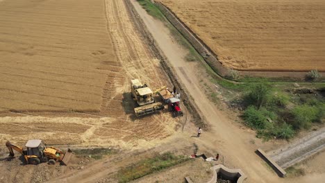 Aerial-Drone-footage-of-a-combine-harvester,-assisted-by-a-tractor,-gathering-wheat