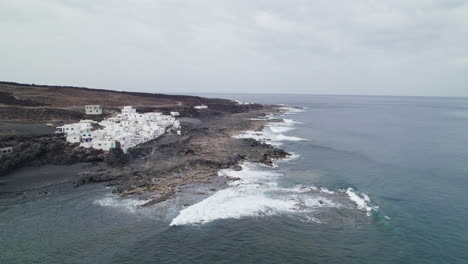 Flying-to-Tenesar-village-in-Lanzarote,-Canary-Islands,-waves-crashing-on-rocks,-white-houses