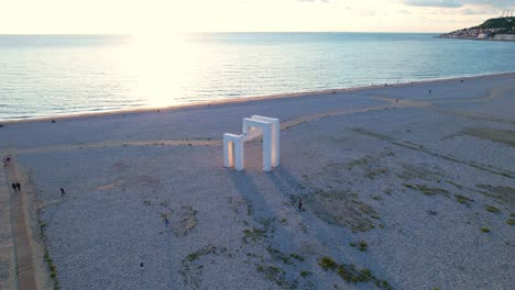 Wunderschönes-Licht-Trifft-Bei-Sonnenuntergang-über-Dem-Meer-Auf-Die-Skulptur-Am-Strand-Von-Le-Havre,-Weitwinkel-Drohnenaufnahme