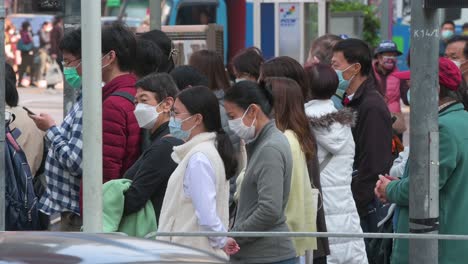 Pedestrians-wait-on-the-sidewalk-for-a-traffic-light-signal-to-turn-green-at-a-zebra-crossing-junction-in-Hong-Kong