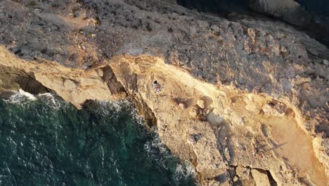 Aerial-top-down-rotating-shot-in-a-rocky-beach-during-sunset-in-Ibiza,-Spain