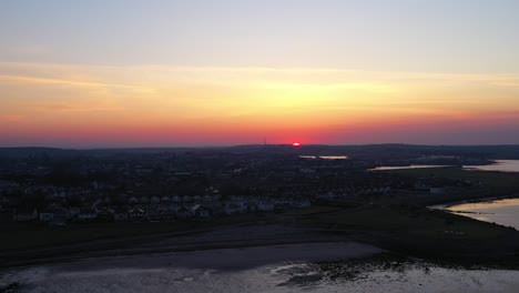 Sun-peaks-above-orange-and-pink-horizon,-Galway-Bay,-Ireland,-aerial-pan