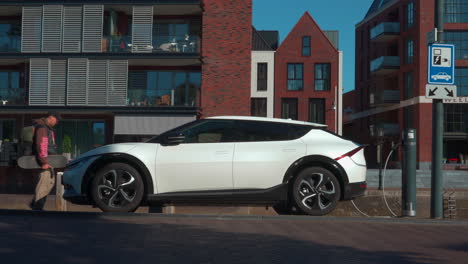 Modern-electric-car-charging-from-a-charging-station-in-a-small-town-centrum,-wide-angle