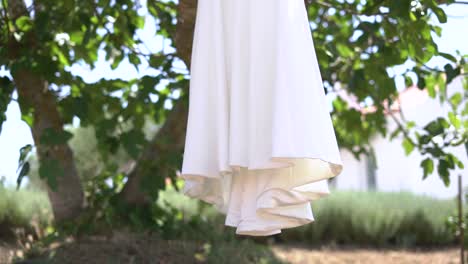 Slow-motion-shot-of-White-Wedding-Dress-Hanging-in-the-garden,-Bottom-detail