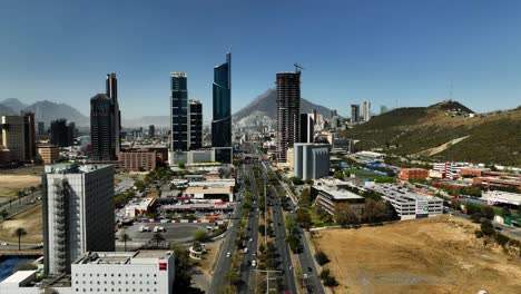 Vista-Aérea-Sobre-El-Tráfico-Que-Sube-Hacia-Los-Rascacielos-En-El-Soleado-San-Pedro-Garza-Garcia,-Monterrey,-México