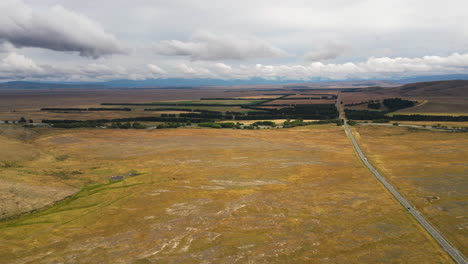 Majestic-vast-plain-crossed-by-highway-by-Lake-Tekapo,-New-Zealand,-aerial-panorama