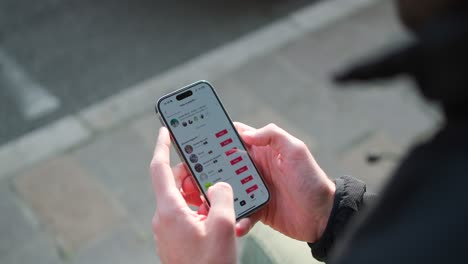 Close-up-of-a-man's-hands-scrolling-through-Instagram-and-other-apps-on-his-iPhone14-while-standing-at-the-side-of-the-street,-capturing-the-reality-of-mobile-technology-in-modern-life