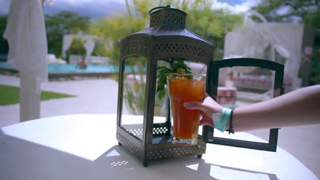 Hand-picks-up-Bloody-Mary-drink-from-cage-by-pool-at-resort,-slo-mo