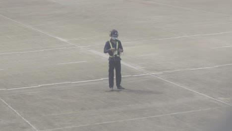 Un-Trabajador-Aeroportuario-Dedicado-En-Uniforme-Se-Encuentra-En-La-Pista-Rodeado-De-Hormigón,-Listo-Para-Ayudar-Al-Piloto-En-El-Despegue