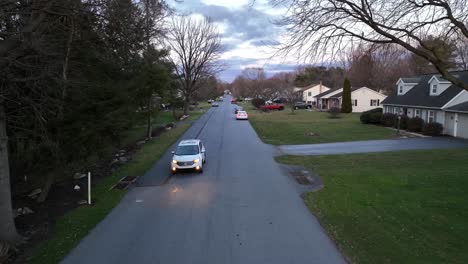 White-Honda-CRV-suv-driving-towards-descending-drone-at-dusk