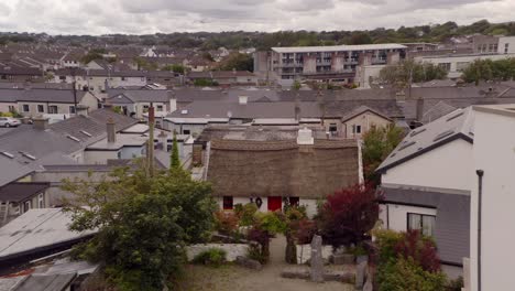 Traditional-Irish-cottage-surrounded-by-modern-houses-in-Claddagh-Galway,-aerial-pullback