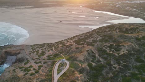 Aerial-establishing-view-high-above-motorhome-parked-on-Bordeira-Portugal-hillside-coastline-overlooking-sunlit-seascape