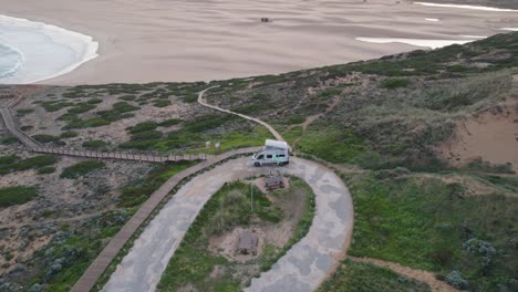 Aerial-orbital-shot-around-a-camper-van-camping-by-the-sea-at-Praia-da-Bordeira-on-the-Algarve-coast-in-Portugal