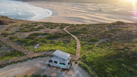 Aerial-landscape-view-during-sunset-of-a-camper-van-near-a-beach-in-Bordeira,-Portugal
