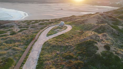 Aerial-establishing-view-of-motorhome-parked-on-Bordeira-Portugal-hillside-coastline-overlooking-sunlit-seascape