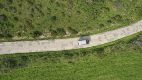 Aerial-Birds-Eye-View-Over-Camper-Van-Driving-Along-Winding-Road-In-Bordeira,-Portugal