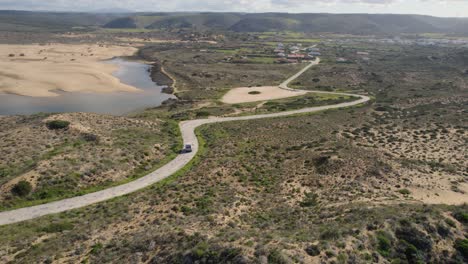 Aerial-view-following-motorhome-travelling-curving-coastal-road-along-Portuguese-beachfront-coastline