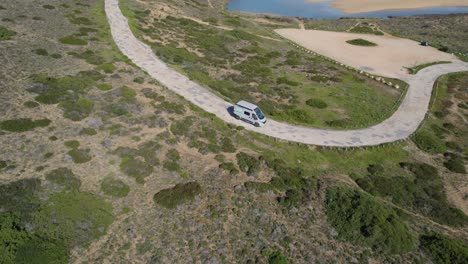 Aerial-tracking-shot-of-a-camper-van-arriving-at-Bordeiras-beach-on-the-coast-of-Algarve-Portugal-at-sunset